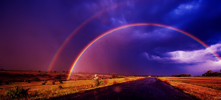 blurred, rainbow in the field rain and dark clouds. Spring season, evening. Panoramic and web banner.の写真素材
