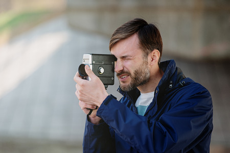 bearded man professional cameraman observes and shoots an 8mm movie camera on a city street in the daytimeの写真素材