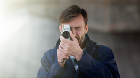 bearded man professional cameraman observes and shoots an 8mm movie camera on a city street in the...