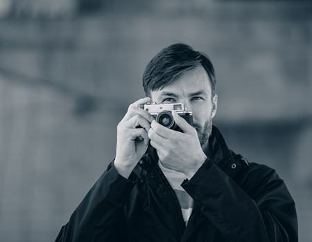 bearded man professional photographer watches and photographs with a film camera on a city street in the daytimeの写真素材