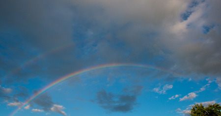RAINBOW AT THE BACKGROUND RAIN CLOUDS. SPRING SEASON IN THE VILLAGE. PANORAMA SKY IN THE SUNNY DAY.の写真素材