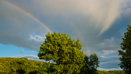 RAINBOW AT THE BACKGROUND RAIN CLOUDS. SPRING SEASON IN THE VILLAGE. PANORAMA SKY IN THE SUNNY DAY.の写真素材