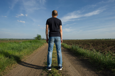 man is standing with his back in the field and staring into the distance at sunset. The traveler is looking into the distance.の写真素材