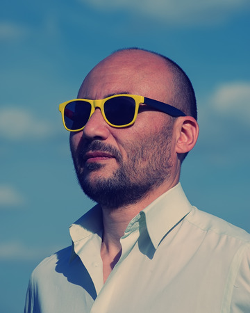 portrait of a businessman in modern sunglasses against a blue sky background. Creative portrait of a man.の写真素材