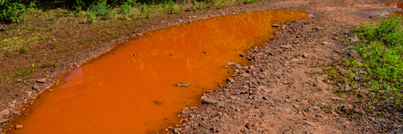 puddle of water painted red with iron salts on a dirt road. Sunny day. Web banner.の写真素材