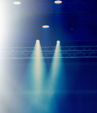 Rays of spotlights illuminate the concert stage with blue light against a dark background. Web...