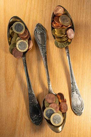 old spoons and euro and eurocent coins lie on the surface of a wooden table. Business concept.の写真素材