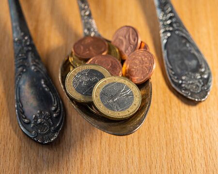 old spoons and euro and eurocent coins lie on the surface of a wooden table. Business concept.の写真素材