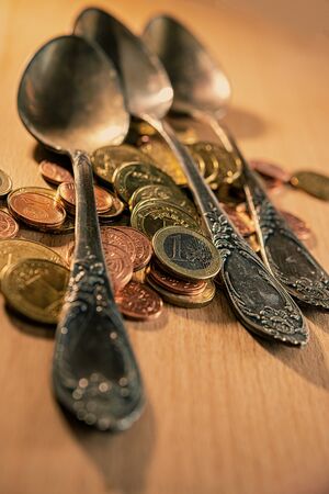 old spoons and euro and eurocent coins lie on the surface of a wooden table. Business concept.の写真素材