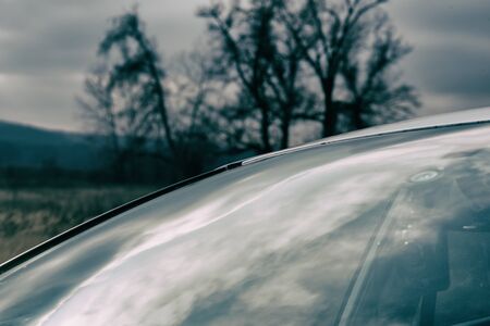 Reflection of the sky on the windshield of a car against a background of dark silhouettes of autumn trees.の写真素材