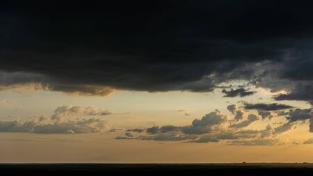 Dramatic dark clouds at sunset and grass silhouettes.