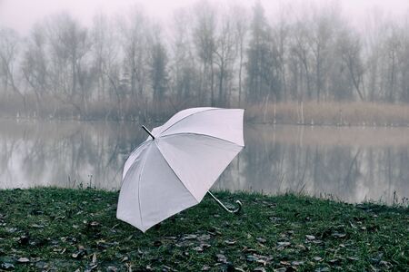 white umbrella lies on the banks of the river in an autumn foggy day.の写真素材