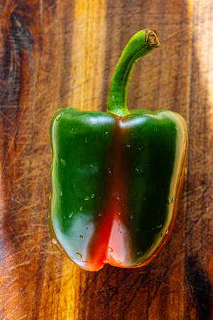 Sweet pepper covered with drops of water lies on an oak board. Summer season.