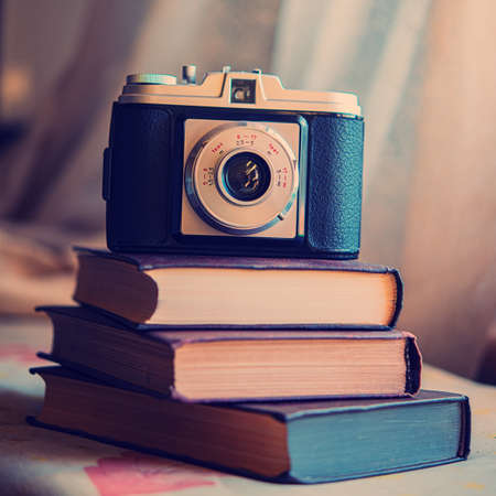 Three vintage books and a film camera are stacked on the table indoors. Books lie on a blurred background.の写真素材