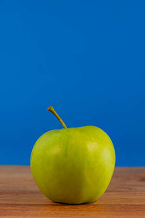 green apple lies on an oak board on a blue background. Background for design.の写真素材