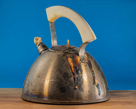 old spoiled burnt teapot lies on an oak board against a blue background. For design.の写真素材