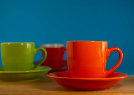 orange, green, red cup in saucers stand on a wooden table against a blue background. For design.の写真素材