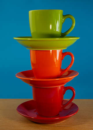 stack of orange, green, red cups in saucers stand on a wooden table on a blue background. For design.の写真素材