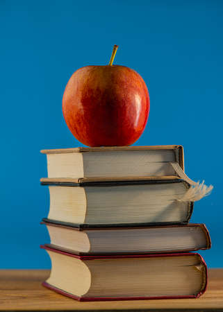 Red apple on a stack of books lying on the surface of an oak table. Creative concept.