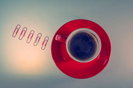red cup with coffee in a saucer stands on a light surface and five paper clips. Business concept....