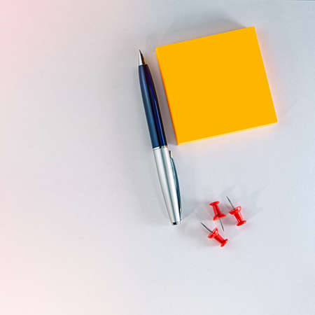 ballpoint pen and stack of orange neon self-adhesive stickers and three red chalkboard pins lie on a light background. Business concept. Cover. Background for text.の写真素材