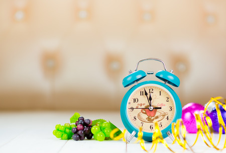 Retro green alarm clock with five minutes to midnight. Decorations grapes christmas balls and ribbons on white table. selected focus.の写真素材