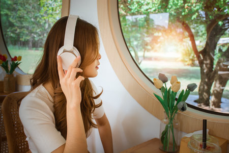 Side view beautiful young woman sitting in cafe with headphone. listening to music & look out of window. Portrait of Asian girl. warm sunlight on winter season. lifestyle vacation happiness concept.の写真素材