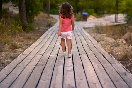 view of a girl walking on a wooden walkway in the middle of the forestの写真素材