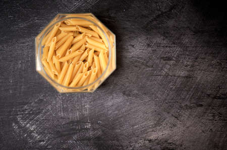 detail of a glass jar with open macaroni pasta on a dark backgroundの写真素材
