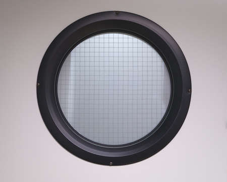 detail of a porthole window with black frame and translucent glass reinforced with wires
