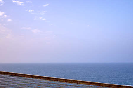detail of a rusted metal railing with the sea and blue sky in the backgroundの写真素材