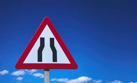 detail of a narrowing traffic sign over a blue cloudy sky