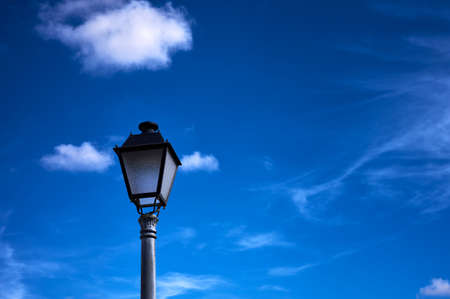 detail of a wrought iron street lamp against a blue and cloudy skyの写真素材