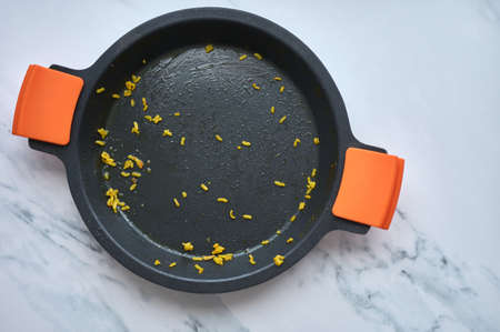 detail of an empty paella pan with leftover rice on a white marble background