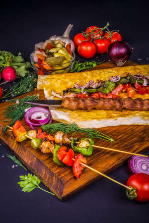 Turkish and Arabic Traditional Ramadan Adana Kebab Roll Wrap serving with vegatable, aubergine salad and hot pepper pickles on rustic wooden background.の写真素材