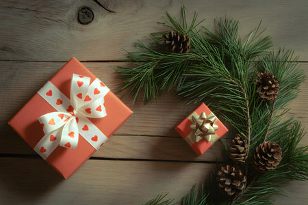 Cozy Christmas scene with a rustic wooden table, featuring a coral gift box with a heart-patterned ribbon, fresh pine branches, and soft lighting for a warm, nostalgic vibe.の素材