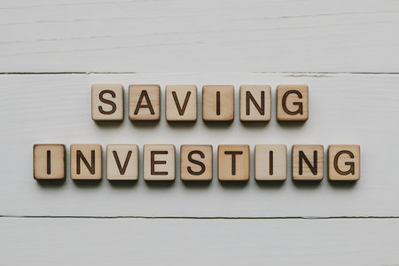 Top-down view of wooden letter tiles spelling âSAVING INVESTINGâ on a light wooden plank. Clean, minimalist composition with natural textures in soft lighting.の素材