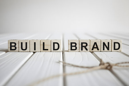Close-up of 'BUILD BRAND' in white wooden letter blocks on a textured white plank. Minimalist design with soft lighting and blurred background, ideal for branding imagery.の素材