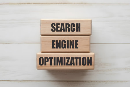 Top-down flat lay of three light wooden blocks stacked with bold text SEARCH, ENGINE, OPTIMIZATION on a white plank background. Minimalist, professional aesthetic.の素材