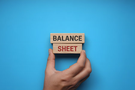 Minimalist flat lay of wooden blocks 'BALANCE' and 'SHEET' on vibrant blue background, symbolizing business strategy and organization in a professional setting.の素材