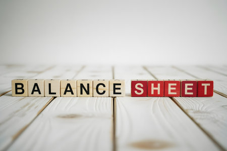 Close-up of 'BALANCE SHEET' in wooden letter blocks on a light textured surface, perfect for finance, accounting, and business-themed visuals.の素材