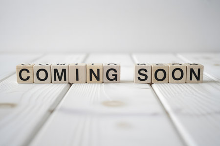 Close-up of 'COMING SOON' in white wooden letter blocks on a blurred white background. Minimalist style with soft lighting and natural shadows.の素材