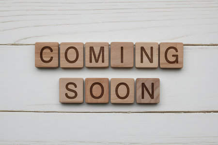 Wooden letter tiles spelling COMING SOON arranged on a light wooden plank background. Minimalist design with soft lighting, highlighting natural textures and clean lines.の素材