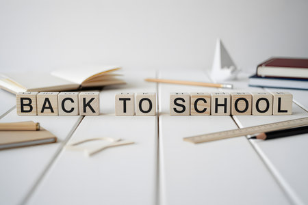 Close-up of 'BACK TO SCHOOL' in white wooden blocks, surrounded by minimal school supplies on a soft, blurred background. Perfect for educational themes.の素材