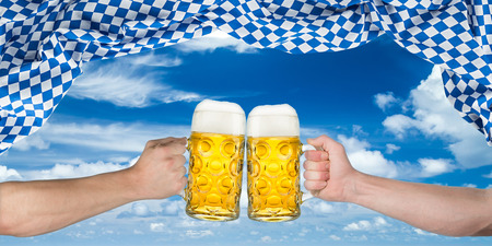 cheers! hands holding up german beer mugs under bavarian flagの写真素材