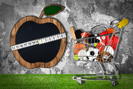 shopping cart filled with sports equipment in front of stone wall with apple shaped blackboardの写真素材