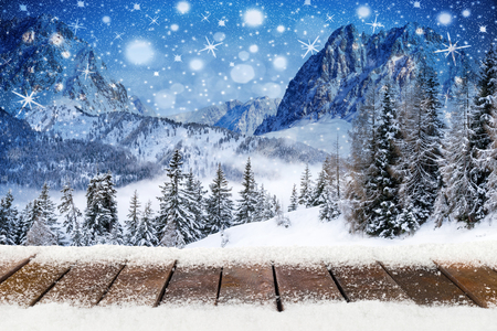 christmas xmas background with wooden snowy planks in front of mountain forest landscape blue night sky with stars and snowflakesの写真素材
