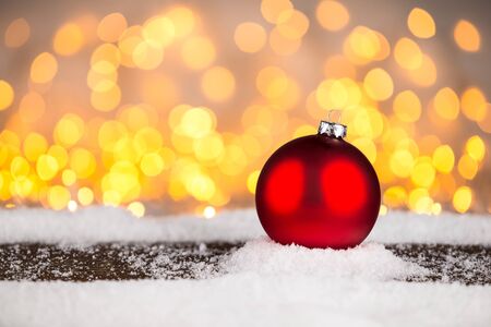 red blank empty christmas xmas bauble ball on snowy wood plank in front of many bright illuminated lights bokeh backgroundの写真素材