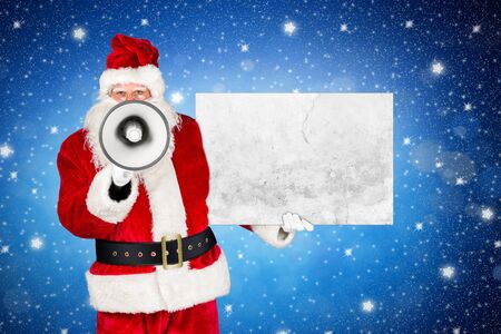 traditional classic red white santa claus making shouting loud announcement with bullhorn megaphone concrete stone sign in his other hand in front of holy night blue stars sky backgroundの写真素材