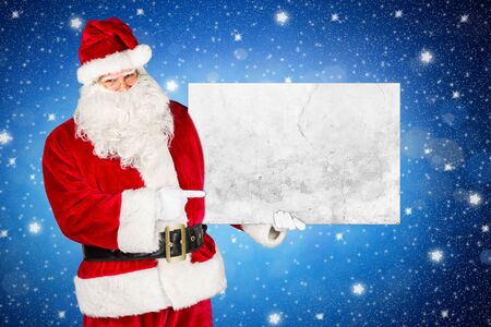 traditional classic red white santa claus making pointing with his finger on concrete stone billboard in his other hand isolated front of blue night sky stars backgroundの写真素材